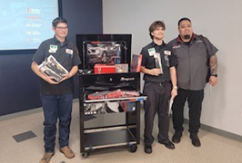  A teacher and two students hold tools and stand in front of a tool chest.